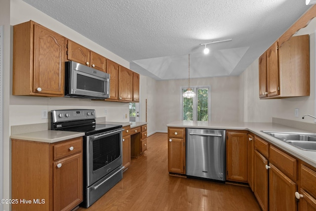 kitchen with a textured ceiling, a peninsula, wood finished floors, a sink, and stainless steel appliances