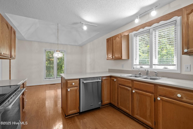 kitchen featuring track lighting, a peninsula, appliances with stainless steel finishes, a sink, and light wood finished floors