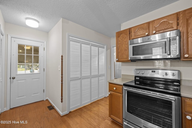 kitchen with light wood-style flooring, brown cabinets, light countertops, and appliances with stainless steel finishes