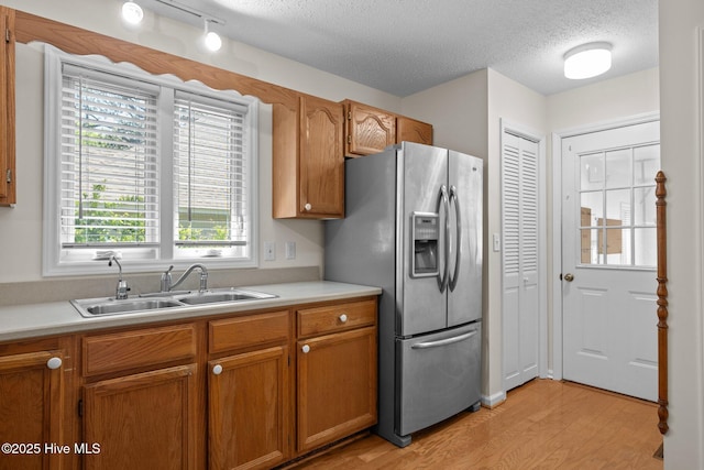 kitchen featuring a textured ceiling, stainless steel refrigerator with ice dispenser, light countertops, a sink, and light wood finished floors