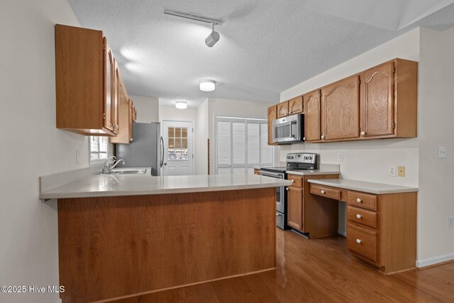 kitchen featuring a peninsula, a textured ceiling, stainless steel appliances, a sink, and wood finished floors