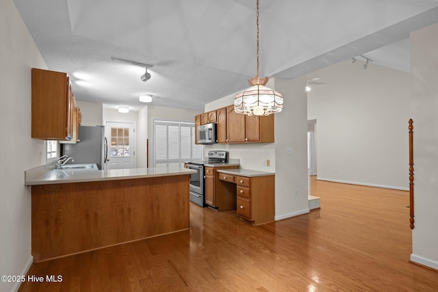 kitchen featuring light wood finished floors, track lighting, brown cabinets, and appliances with stainless steel finishes