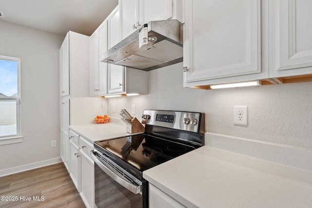 kitchen featuring stainless steel electric range oven, light countertops, light wood-type flooring, under cabinet range hood, and white cabinetry