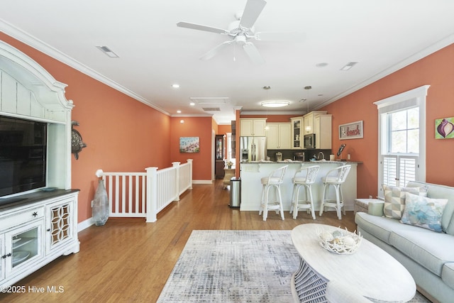 living area with recessed lighting, ornamental molding, light wood finished floors, baseboards, and visible vents
