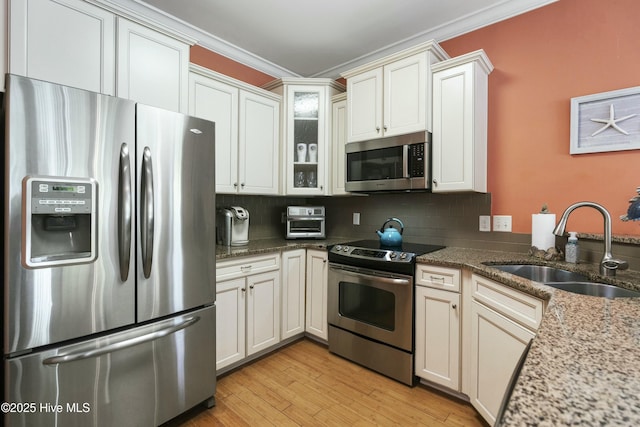 kitchen with a sink, tasteful backsplash, light stone counters, ornamental molding, and appliances with stainless steel finishes
