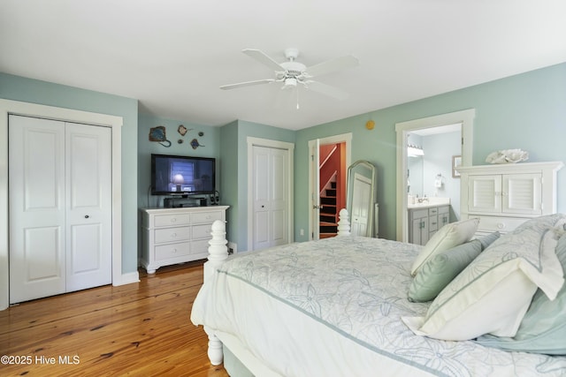 bedroom featuring two closets, ceiling fan, ensuite bath, baseboards, and wood finished floors