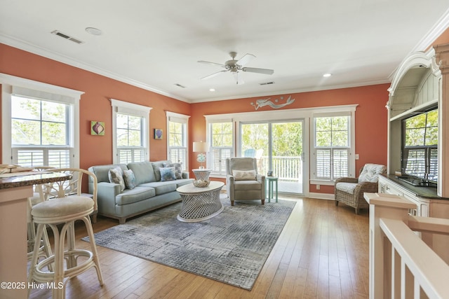 living area featuring a wealth of natural light, visible vents, ceiling fan, and crown molding