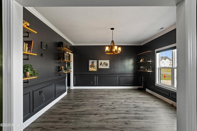 unfurnished dining area featuring ornamental molding, a chandelier, a textured ceiling, dark wood-type flooring, and visible vents