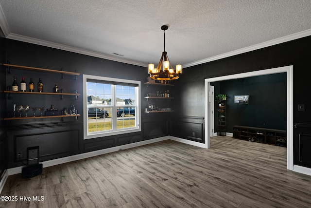 unfurnished dining area with a chandelier, a textured ceiling, wood finished floors, and ornamental molding