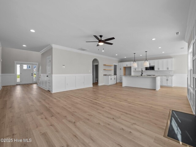 unfurnished living room featuring recessed lighting, a sink, arched walkways, light wood-style flooring, and ceiling fan