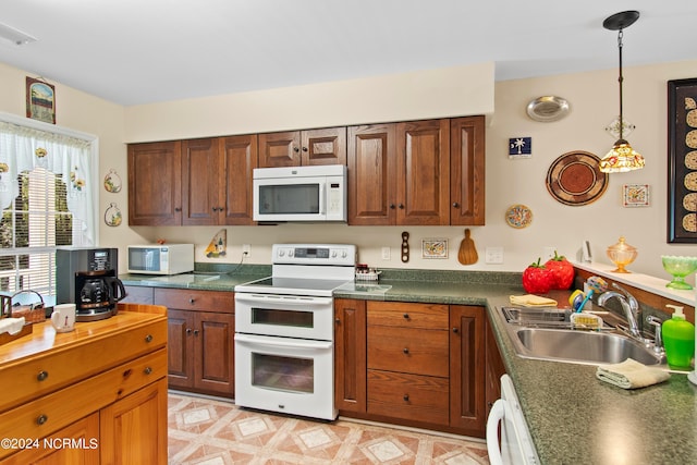 kitchen featuring white appliances, visible vents, a sink, dark countertops, and hanging light fixtures
