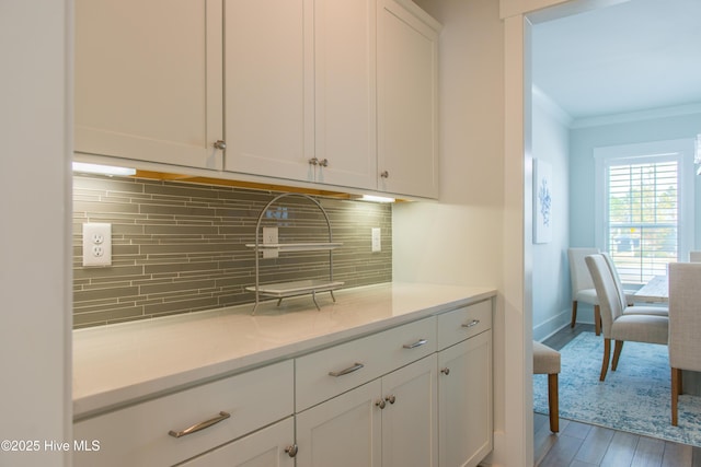 kitchen featuring white cabinets, light wood finished floors, light countertops, decorative backsplash, and ornamental molding