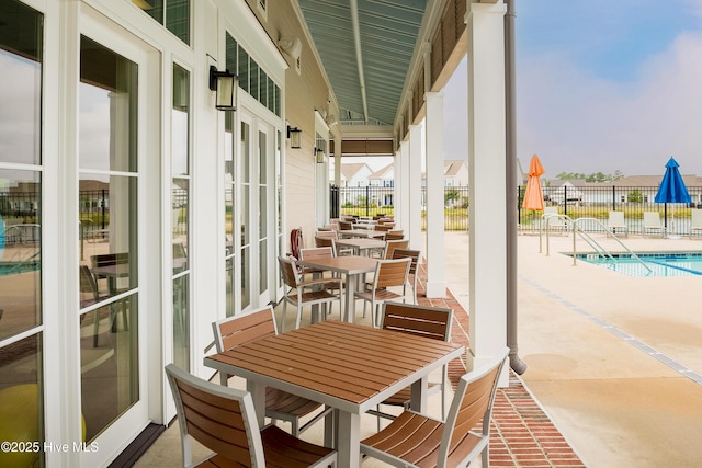 view of patio with fence, outdoor dining space, and a community pool