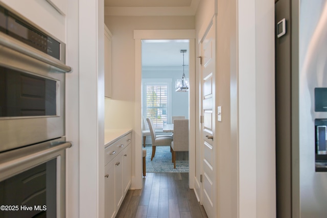 hall with dark wood-type flooring, a chandelier, and ornamental molding