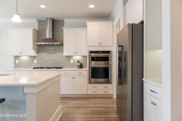 kitchen with stainless steel appliances, wall chimney range hood, white cabinets, light countertops, and recessed lighting
