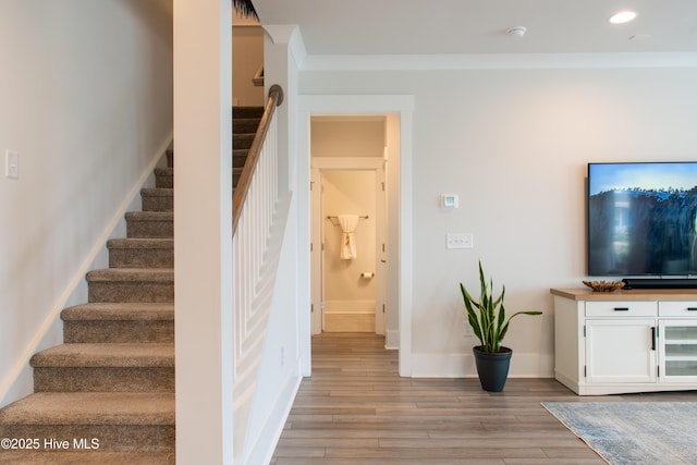 stairway featuring wood finished floors, baseboards, recessed lighting, and crown molding