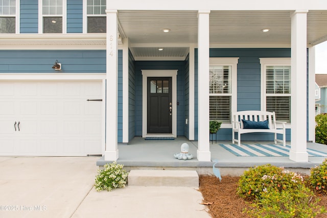 doorway to property featuring a porch, concrete driveway, and an attached garage