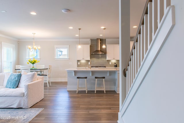 kitchen with wall chimney range hood, a breakfast bar area, ornamental molding, light countertops, and open floor plan