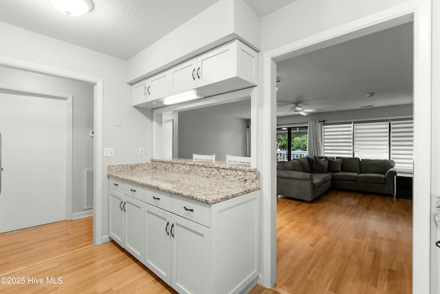 kitchen with a ceiling fan, white cabinetry, light wood-style flooring, light stone countertops, and a textured ceiling