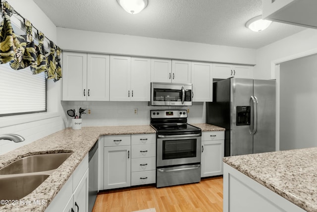 kitchen with stainless steel appliances, a sink, light wood-type flooring, a textured ceiling, and light stone counters