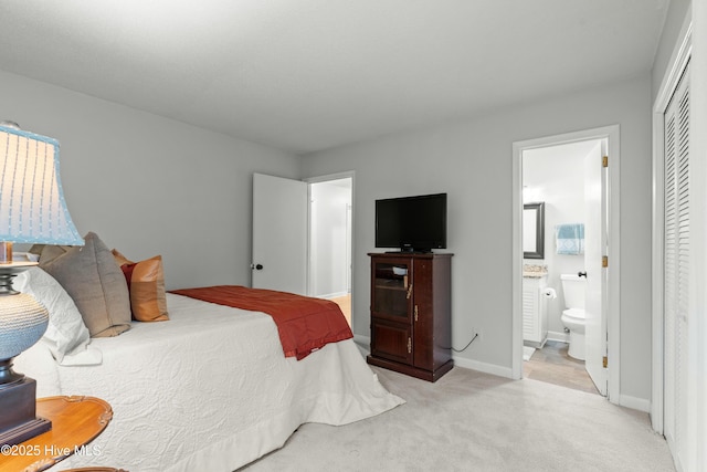 bedroom with ensuite bath, light carpet, a closet, and baseboards