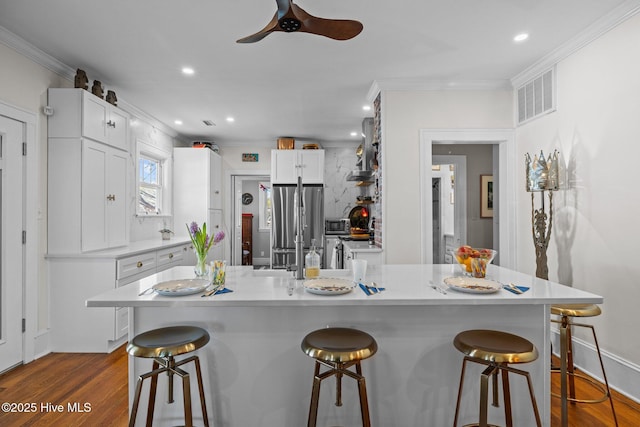 kitchen with visible vents, freestanding refrigerator, a breakfast bar area, and ornamental molding