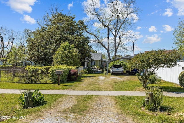 view of front of house featuring fence, a carport, a front yard, and dirt driveway