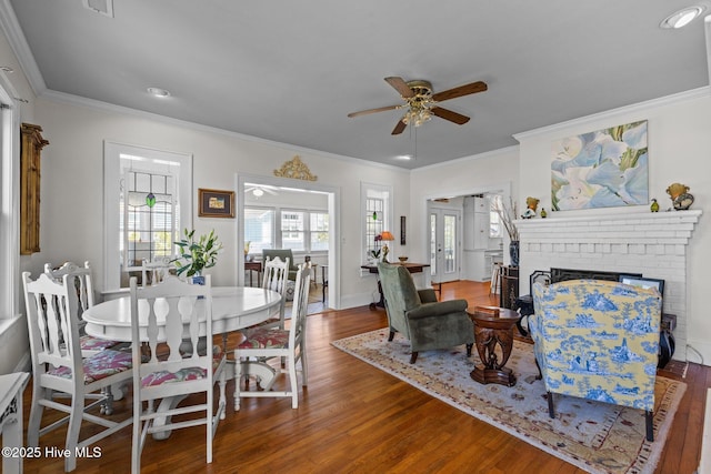 dining room with a ceiling fan, a brick fireplace, and wood finished floors