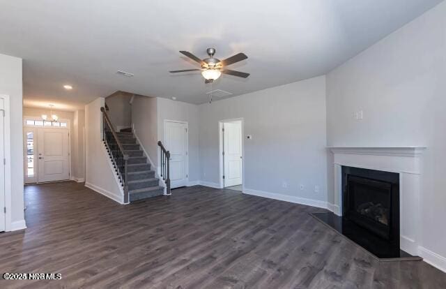 unfurnished living room with stairs, dark wood-type flooring, a fireplace with raised hearth, and baseboards