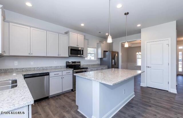 kitchen with pendant lighting, recessed lighting, a kitchen island, appliances with stainless steel finishes, and dark wood-style flooring