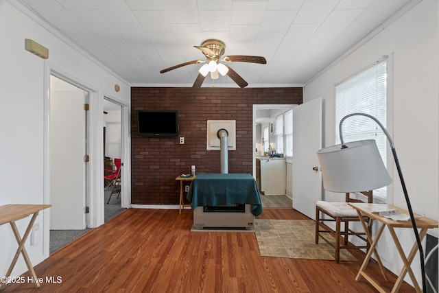 sitting room featuring brick wall, a wood stove, wood finished floors, and ceiling fan