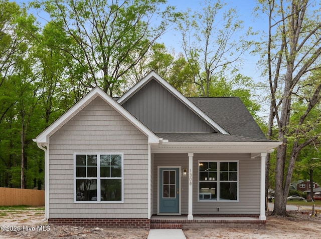view of front of property featuring roof with shingles, fence, covered porch, and board and batten siding