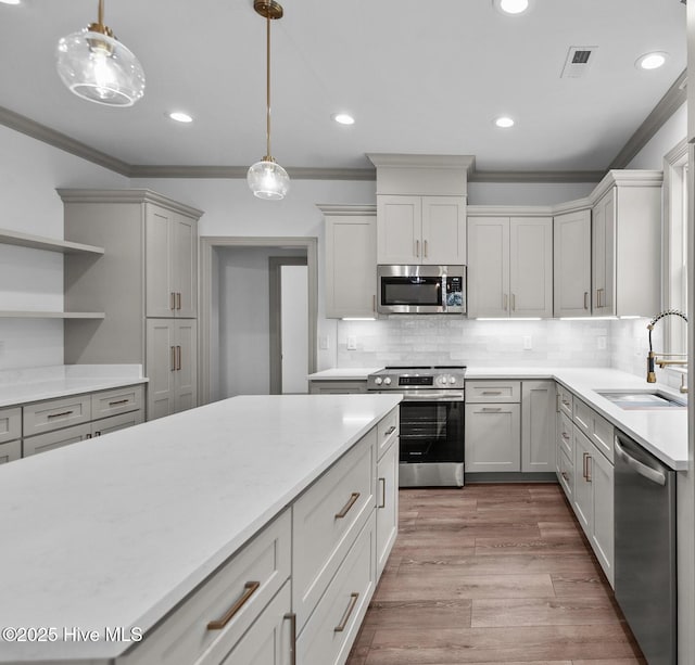 kitchen with decorative light fixtures, visible vents, appliances with stainless steel finishes, a sink, and ornamental molding