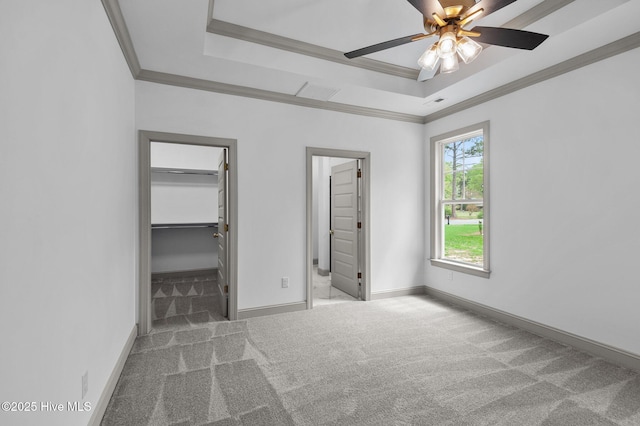 unfurnished bedroom featuring carpet floors, a raised ceiling, crown molding, and a walk in closet