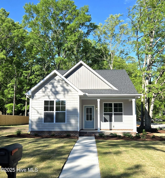 bungalow-style house featuring fence, a front yard, a shingled roof, board and batten siding, and a porch