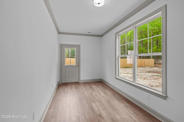 empty room with light wood-style floors, ornamental molding, and baseboards