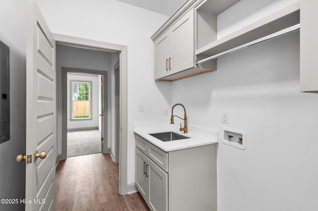 laundry area with cabinet space, a sink, hookup for a washing machine, baseboards, and wood finished floors