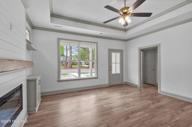 unfurnished living room featuring ornamental molding, a raised ceiling, light wood finished floors, and a large fireplace