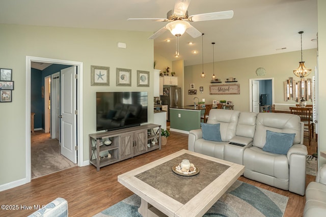 living room featuring ceiling fan with notable chandelier, wood finished floors, baseboards, and vaulted ceiling