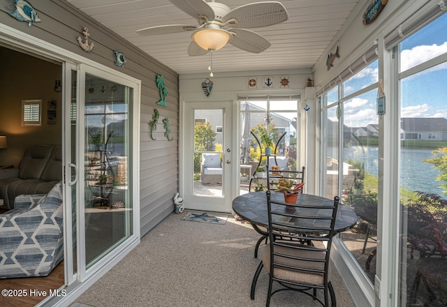 sunroom with a ceiling fan and a water view