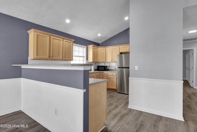 kitchen with freestanding refrigerator, black microwave, light brown cabinetry, visible vents, and a wainscoted wall