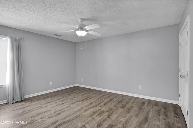 unfurnished room with visible vents, ceiling fan, wood finished floors, and baseboards