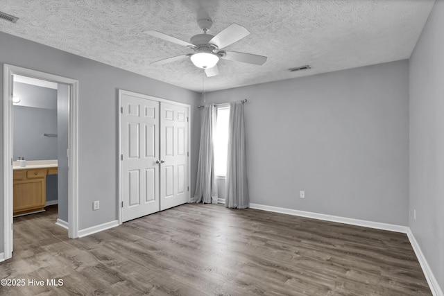 unfurnished bedroom with a closet, baseboards, a textured ceiling, visible vents, and wood finished floors