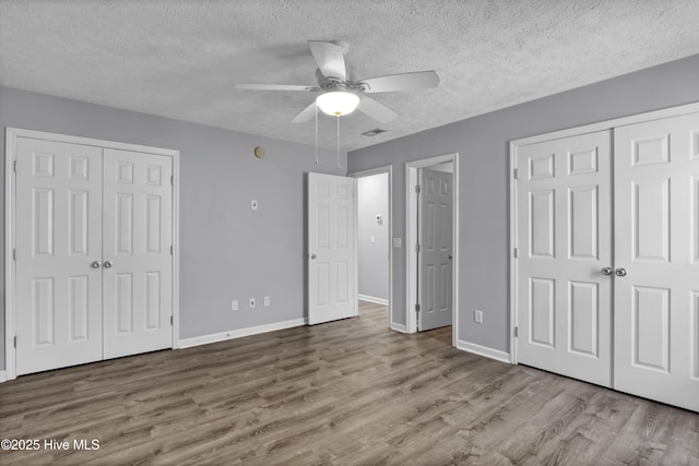 unfurnished bedroom featuring two closets, wood finished floors, baseboards, and a textured ceiling