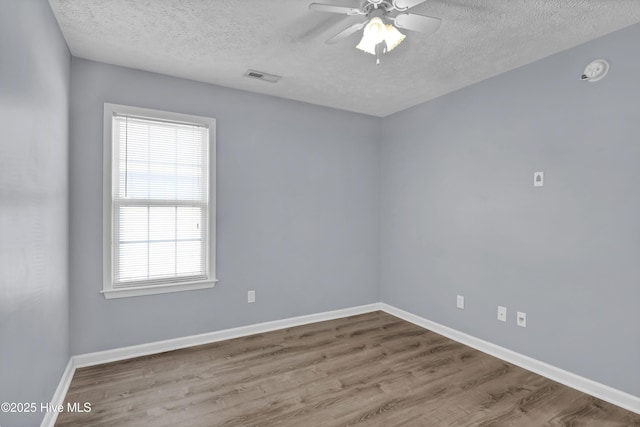 spare room featuring baseboards, a textured ceiling, a ceiling fan, visible vents, and wood finished floors