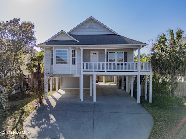 coastal home featuring a carport, concrete driveway, roof with shingles, and covered porch