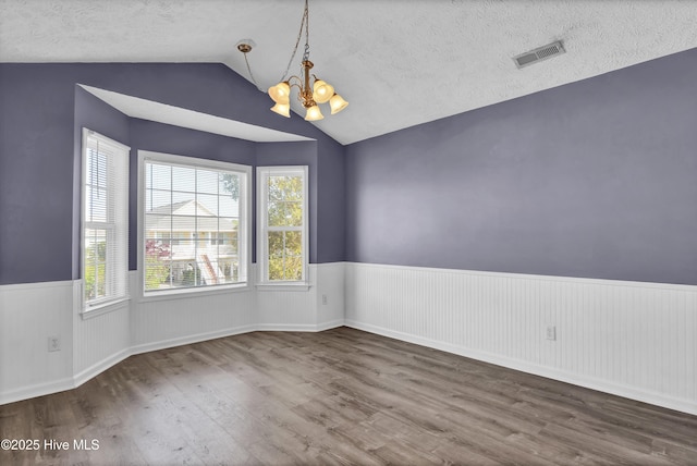 spare room with an inviting chandelier, a wainscoted wall, visible vents, lofted ceiling, and wood finished floors