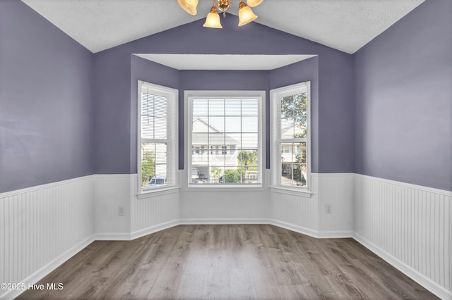empty room with a wainscoted wall, a ceiling fan, wood finished floors, and lofted ceiling
