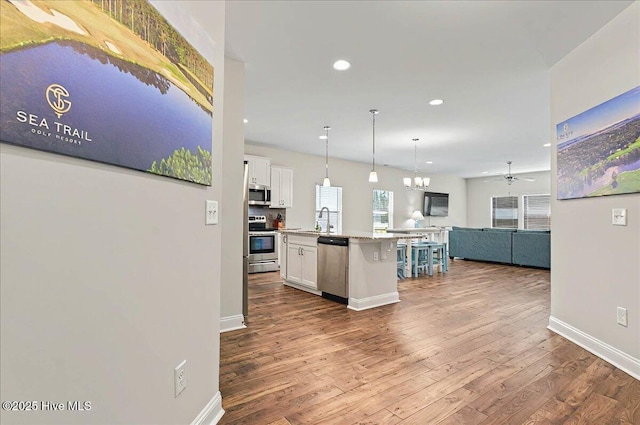 kitchen with recessed lighting, open floor plan, wood finished floors, white cabinets, and appliances with stainless steel finishes