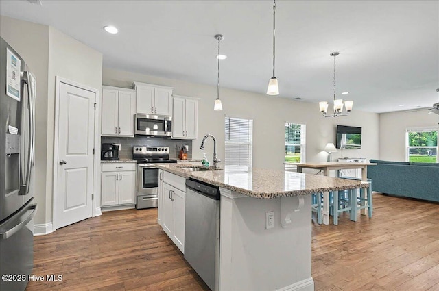 kitchen with a sink, stainless steel appliances, open floor plan, white cabinets, and light stone counters